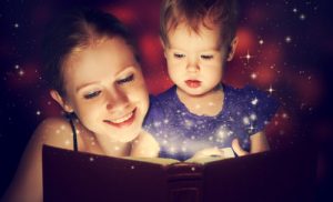 family mother and child baby daughter reading magic book in the dark